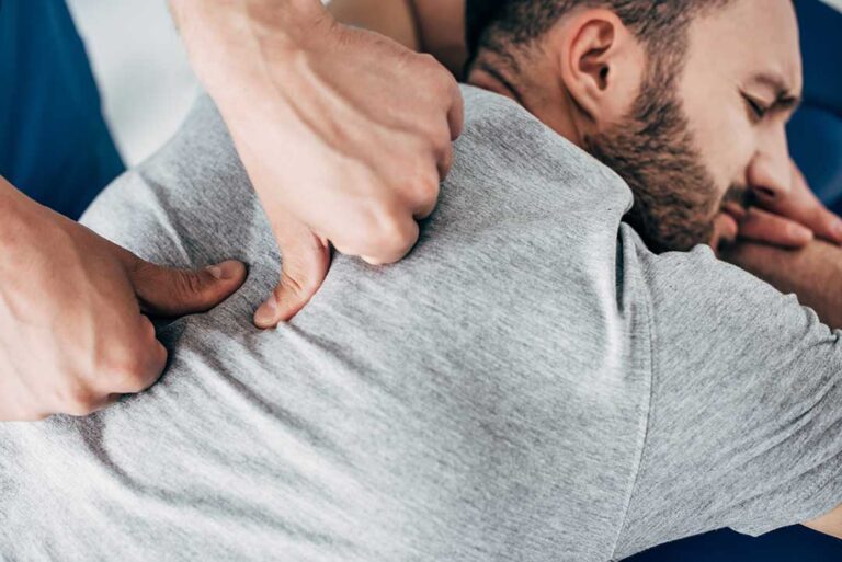 A chiropractor performs gentle spinal manipulation on an adult patient in a bright clinic room.