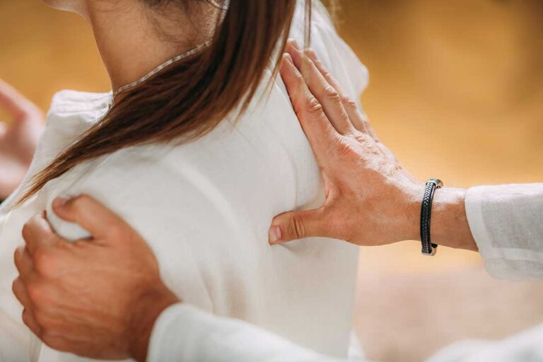 A middle-aged person gently rotating their arm while checking for shoulder movement in a bright, simple home setting.